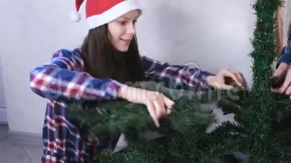 快乐的妈妈和儿子戴着圣诞帽在家里安装圣诞树为圣诞节做准备视频的预览图