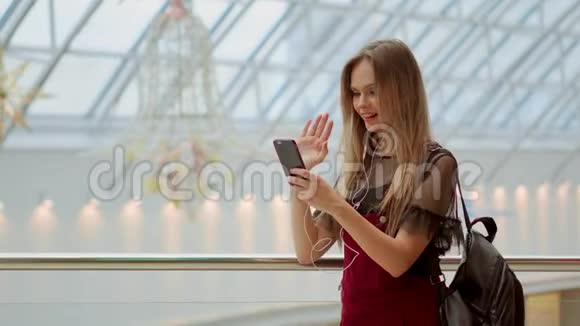 女孩带着一个背包通过耳机和一部手机在机场的视频拼贴上交谈摆姿势自拍视频的预览图