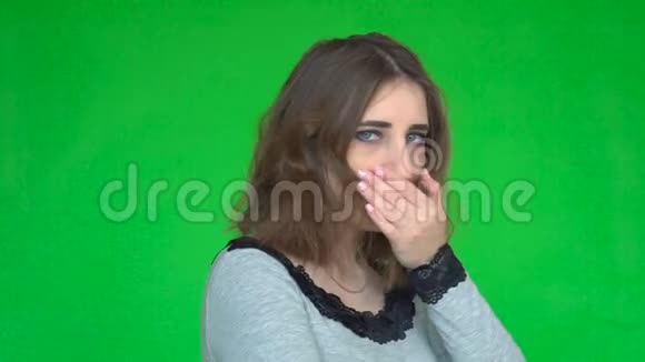 年轻女子一边用手掌咳嗽一边看着绿色背景上的相机视频的预览图