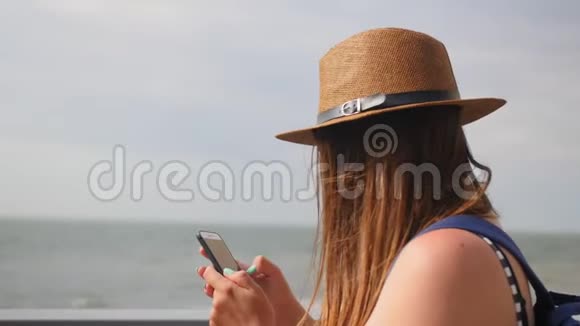 侧景特写年轻女孩戴着帽子在夏天的长廊散步在智能手机上拍照享受散步视频的预览图