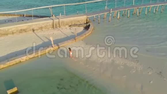 4小岛上一名女子独自步行前往码头在孤零零的白色沙洲上用木制长臂木作支撑视频的预览图