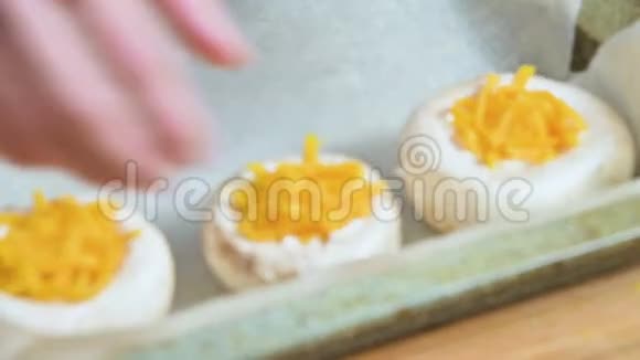 在烹饪过程中女性双手在烤盘上撒满奶酪的蘑菇视频的预览图