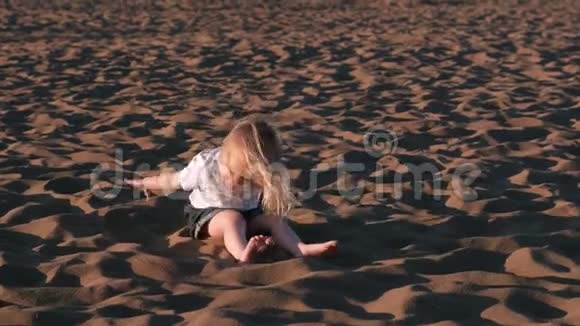 美丽快乐的小女孩金发女郎在海滩上玩耍和扔沙视频的预览图