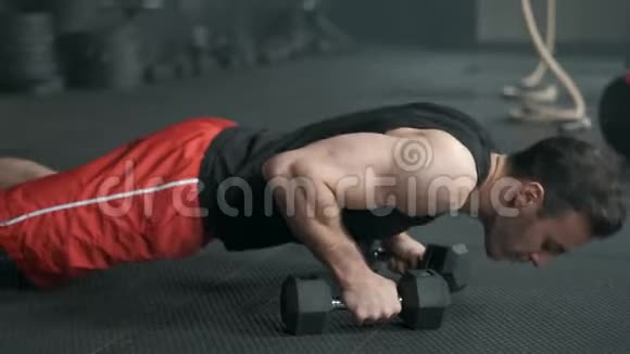 这个肌肉发达的人正在用哑铃做俯卧撑运动进行交叉配合的锻炼4K慢动作视频的预览图