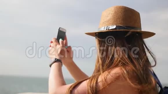 侧景特写年轻女孩戴着帽子在夏天的长廊散步在智能手机上拍照享受散步视频的预览图
