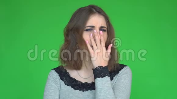疲惫的年轻女子打着哈欠捂住嘴看着绿色背景上的相机视频的预览图