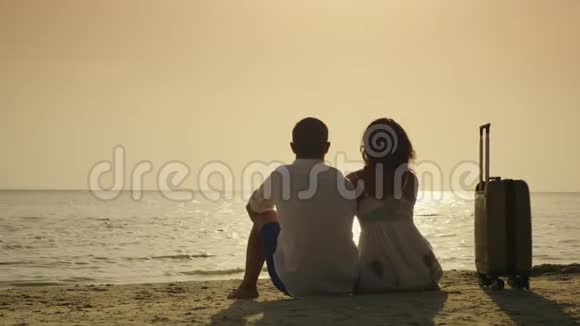 抵达度假一对年轻夫妇坐在旅行袋附近的沙滩上欣赏大海上的日落视频的预览图