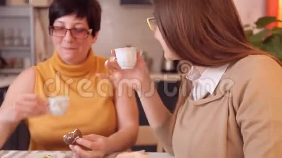 妈妈和女儿带着眼镜看电视上的新闻喝茶或咖啡出了点事女儿打电话视频的预览图