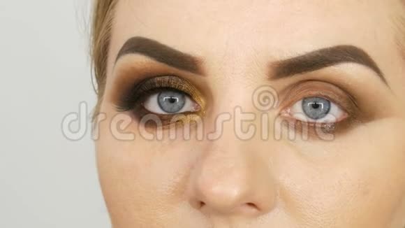 大师化妆师在美容院将专业化妆的金色烟雾眼睛应用于一个蓝眼睛的胖女人模特视频的预览图