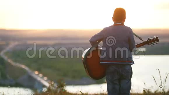 戴着圆眼镜的男孩在夕阳下的田野里弹吉他望向水平视频的预览图