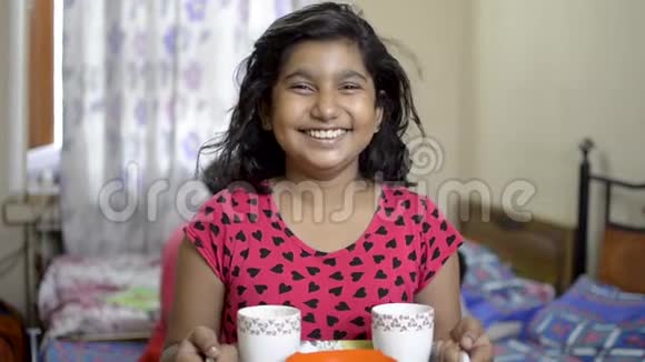 可爱的小快乐的印度白人女孩抱着茶杯和小吃在托盘前视图肖像视频的预览图