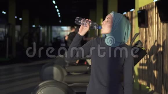 年轻运动的穆斯林女孩戴着头巾锻炼后从瓶子里喝水慢节奏视频的预览图