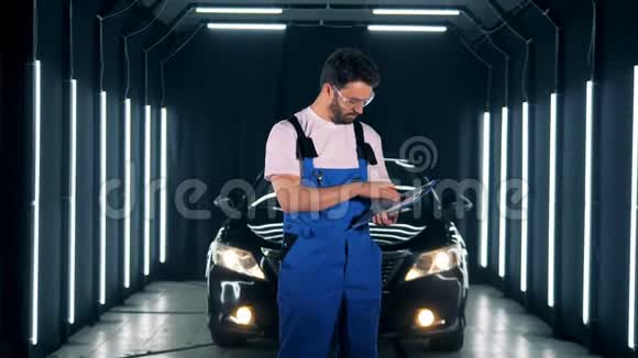 修理工在汽车背景上的剪贴板上写字工人站在车库里拿着剪贴板写字视频的预览图