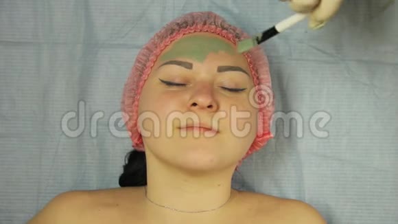 一位戴手套的男性美容师将带刷子的泥面罩涂在女性客户的脸上视频的预览图
