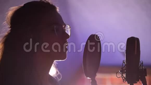 一位戴着眼镜和耳机的年轻女子站在麦克风旁唱歌视频的预览图