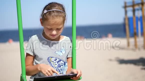 肖像画十几岁的孩子长发金发的金发女孩在平板电脑上工作在海滩上在炎热的夏天对抗着视频的预览图