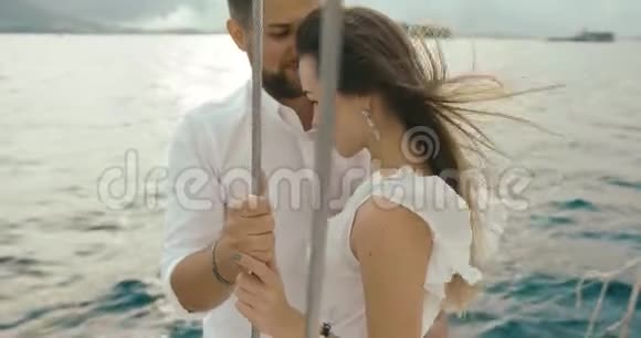 恋爱中的情侣在游艇上放松风吹着女人衣服而男人则站在白色游艇上拥抱她的温柔视频的预览图