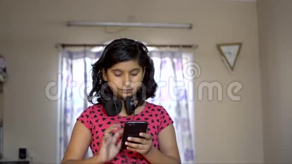 印度白种人女孩忙于电话检查文本耳机在脖子上音乐爱好者正面视图的肖像视频的预览图