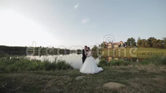 白人新郎和新娘在湖边的公园里新婚夫妇新婚夫妇接吻视频的预览图