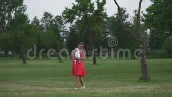 年轻的母亲抱着她的孩子在城市公园玩耍她站在那里穿着鲜红的裙子儿子穿着视频的预览图