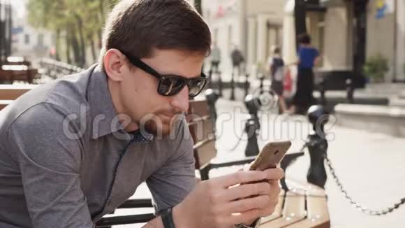 戴墨镜的商人用智能手机在城市阳光明媚的早晨工作视频的预览图