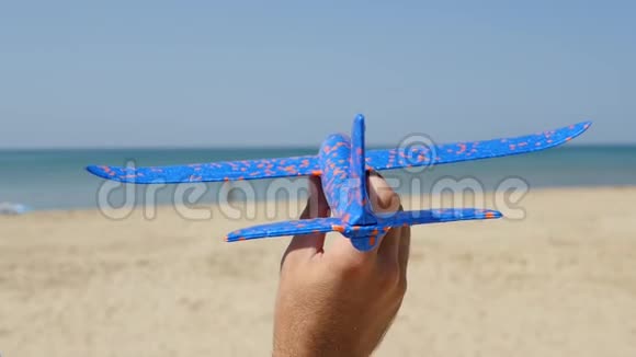 一个人的手在一个炎热的阳光明媚的日子里在大海的背景上拿着一架玩具飞机一个人发射一架飞机特写镜头视频的预览图