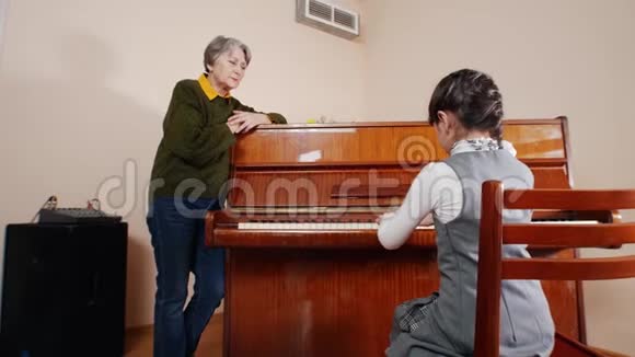 音乐课女孩弹钢琴年长的老师站在钢琴附近帮助弹钢琴斜视图视频的预览图