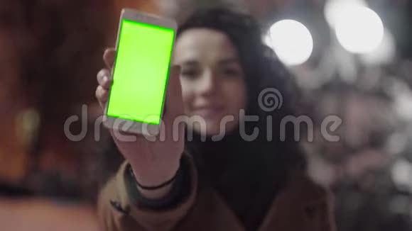 年轻女孩正拿着绿色屏幕的智能手机晚上竖起大拇指休闲生活方式视频的预览图