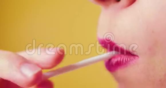 一个嘴唇粉红色的女人甜美地舔一个棒棒糖喜欢吃糖果黄色背景工作室性感特写嘴巴视频的预览图