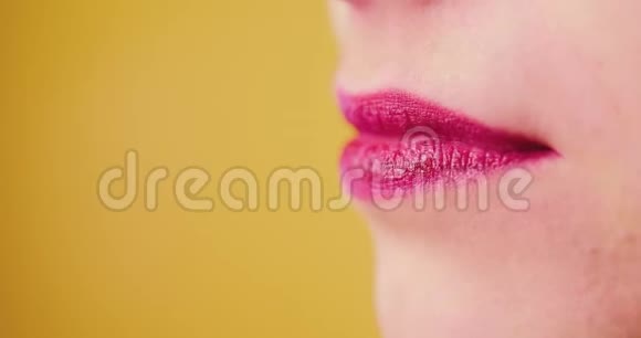 一个嘴唇粉红色的女人甜美地舔一个棒棒糖喜欢吃糖果黄色背景工作室性感特写嘴巴视频的预览图