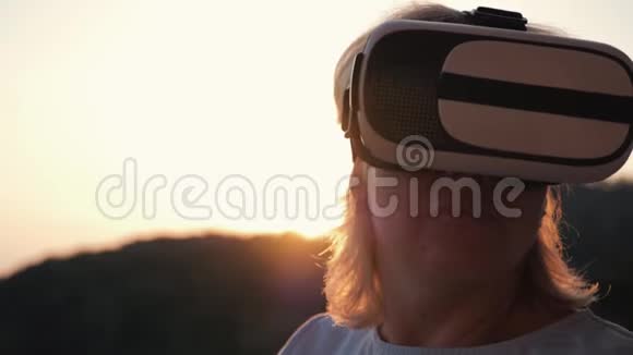 日落时戴着虚拟现实眼镜的金发女孩现代技术虚拟生活和交流视频的预览图
