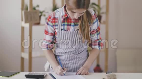 小生意一个穿着条纹围裙和格子衬衫的女孩站在一家花店里这个女孩正在计算视频的预览图