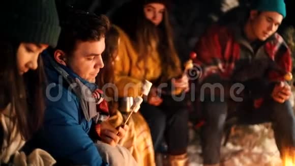 一群年轻人在冬林中坐在火边在火边给马什梅洛热身视频的预览图