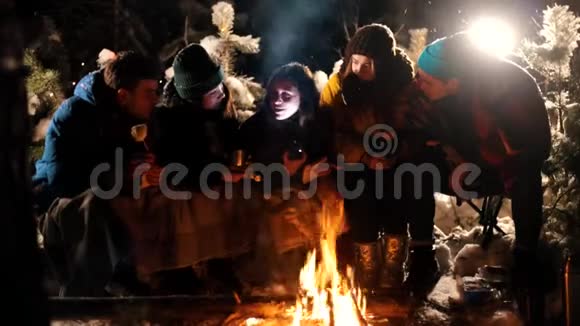 群年轻人坐在冬天的森林里的火边一个年轻的女人给她的朋友讲了一个可怕的故事抱着一个可怕的故事视频的预览图