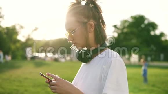 侧面看一个穿白色T恤的漂亮女孩在手机上打字她脖子上戴着黑色耳机花费时间视频的预览图