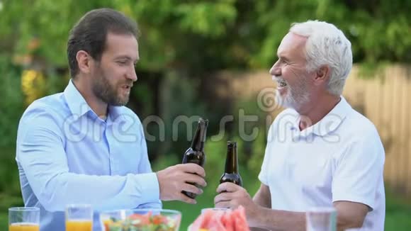 年长和中年男子在啤酒瓶上叮当作响谈论着酿造的传统视频的预览图