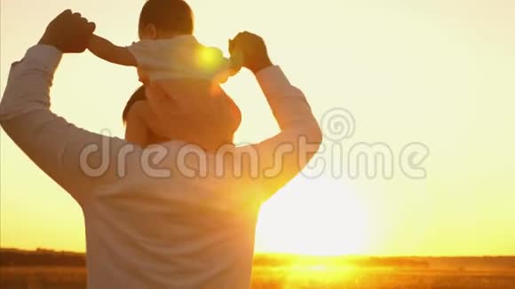 太阳落山时爸爸抱着宝宝坐在肩上夏天在公园散步的幸福家庭特写视频的预览图