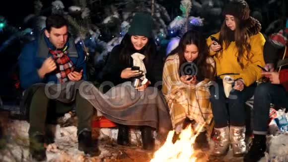 冬天森林里的年轻人坐在火边人们坐在手机里微笑社会问题视频的预览图