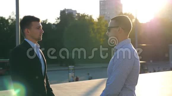 两个年轻的商人站在城市广场户外聊天商人们在外面与城市景观打交道视频的预览图