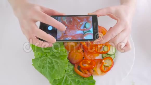 女人用智能手机白色盘子上的新鲜蔬菜沙拉拍照视频的预览图