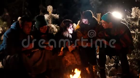 群年轻人坐在冬天的森林里的火边一个年轻的女人给她的朋友讲了一个可怕的故事抱着一个可怕的故事视频的预览图