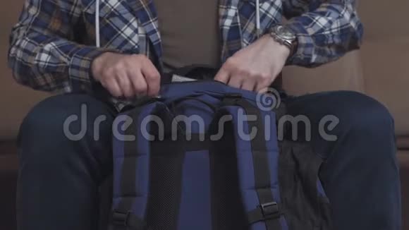 一个男人坐在沙发上把东西放在背包里把它系紧然后离开框架视频的预览图