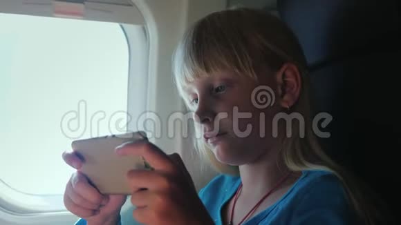 一个金发女孩坐飞机在智能手机上玩视频的预览图