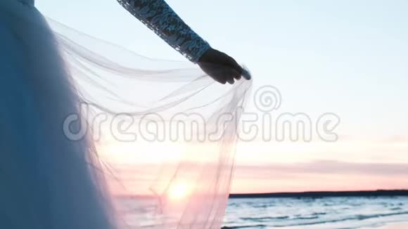 女人手里的蕾丝袖子握着婚纱的下摆日落时随风飘扬的透明织物视频的预览图