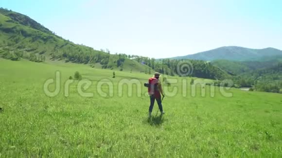 那个女人带着旅游棒和一个红色背包爬上了一座绿色的山然后女人坐在上面视频的预览图