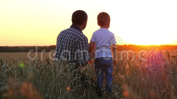 一个农夫和他的儿子在日落背景下的麦田里爸爸和孩子很高兴看到视频的预览图
