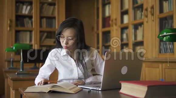 勤奋的女学生生物学家在图书馆用书和笔记本电脑在桌子上写作视频的预览图