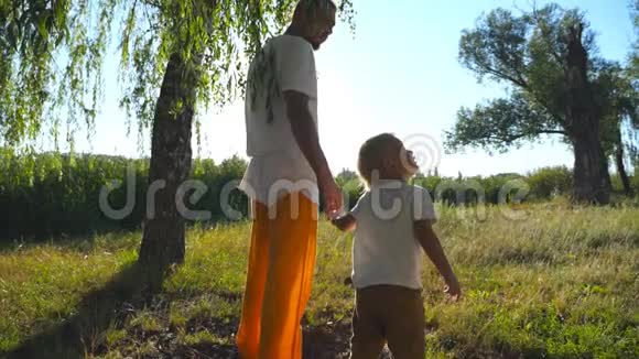 在夏天和爸爸一起穿过绿色公园的时候小孩子抬头看着一棵高大的树年轻的父亲和可爱的视频的预览图