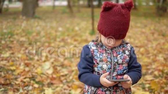 女孩在黄叶的背景下看着电话秋天视频的预览图