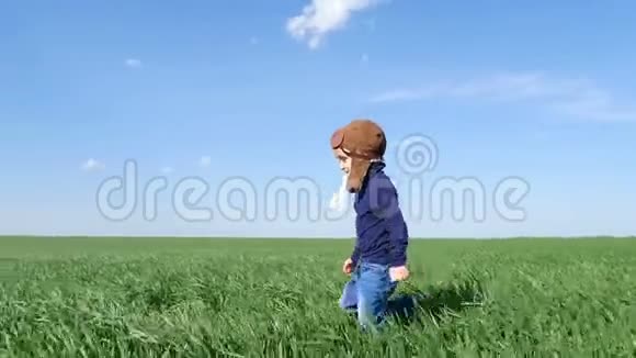 一个穿着飞行员西装快乐的孩子沿着绿色的田野奔跑他的双手缓慢地在飞机上飞行视频的预览图